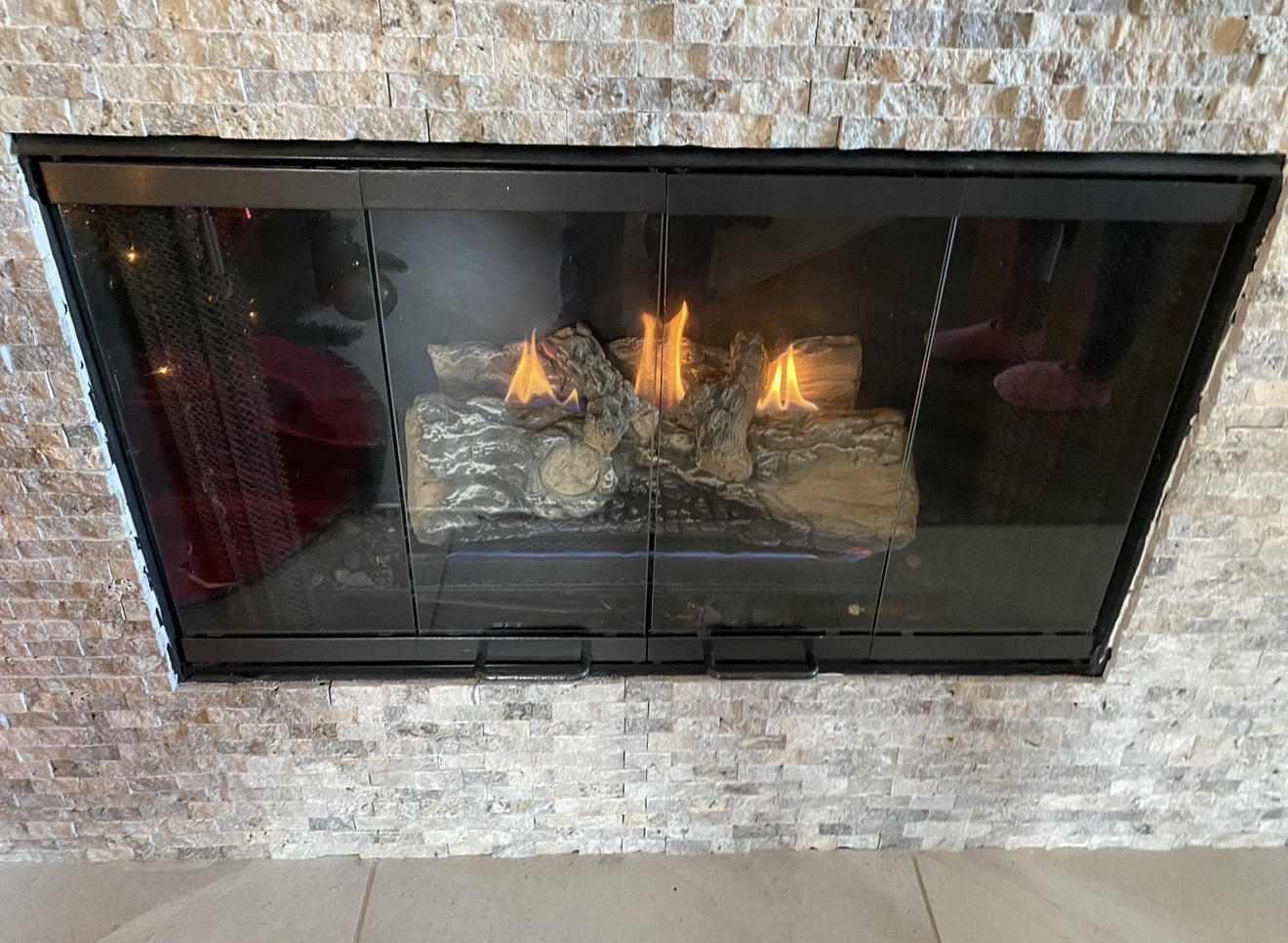 Gas fireplace with burning logs and a textured stone surround at a Fireside Escapes service project in Frisco